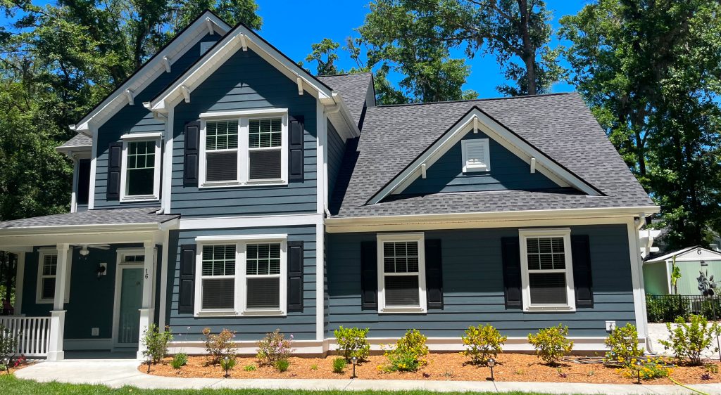 A two-story blue house with white trim, a covered porch, and a landscaped front yard under a clear blue sky.